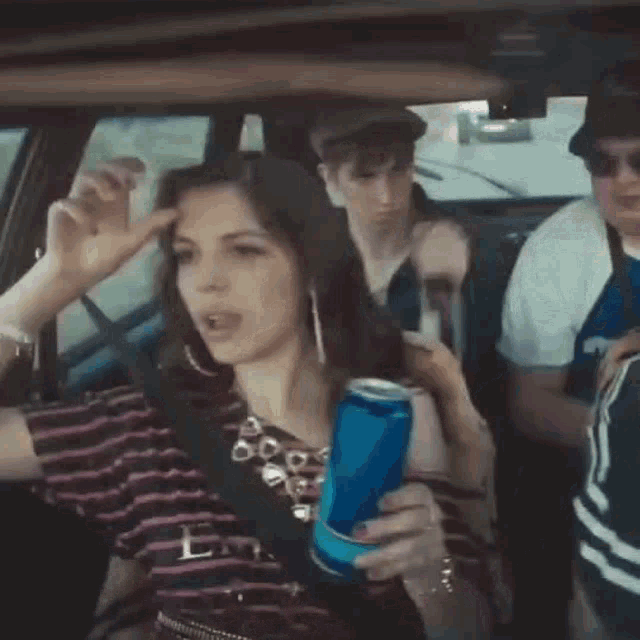 a woman is holding a can of soda while sitting in a car with other people .