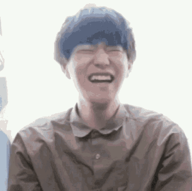 a young man in a brown shirt is laughing with his mouth open .