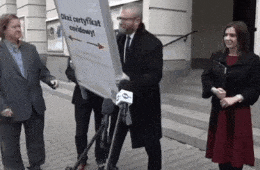 a man in a suit is holding a sign that says " okaz certyfikat covidowy "