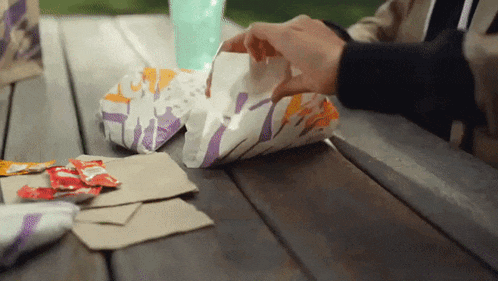 a person sitting at a picnic table eating taco bell food