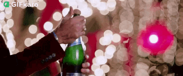 a man in a suit is opening a bottle of champagne in front of a christmas tree .