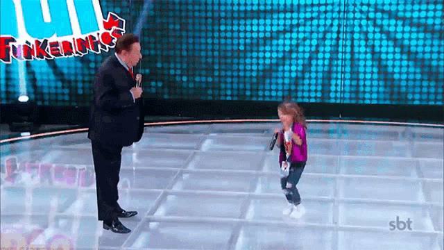 a little girl is singing into a microphone while a man stands behind her in front of a screen that says funkados