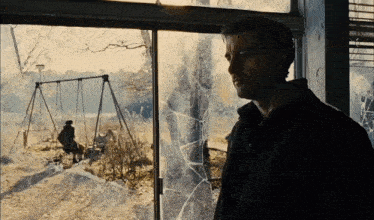 a man stands in front of a broken window with a swing set behind him
