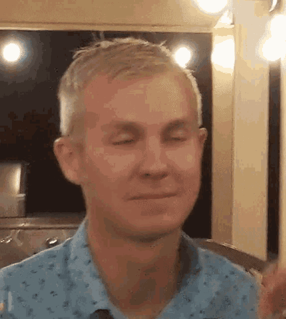 a man wearing a blue shirt is making a funny face with his eyes closed