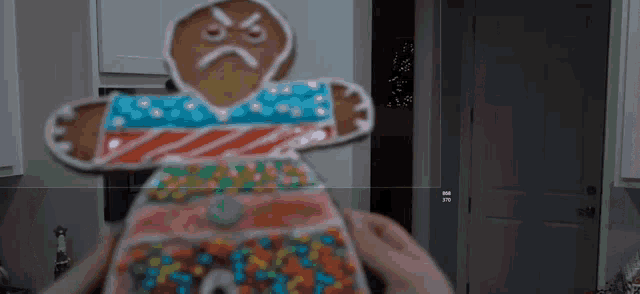 a person is holding a gingerbread man decorated with candy and icing .