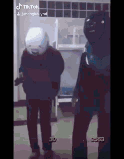 a couple of people are standing next to each other in a room . one of the people is wearing a helmet .