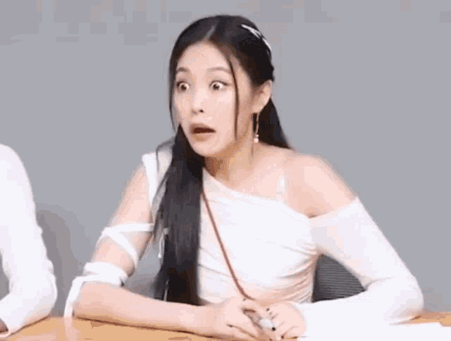 a woman is sitting at a table with her mouth open and a surprised look on her face .