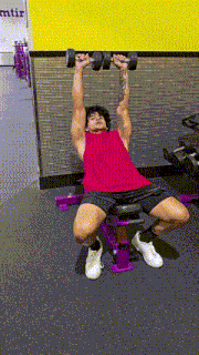 a man is sitting on a bench in a gym lifting a dumbbell .