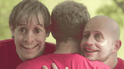 three men are hugging each other and one of them has a bald head .