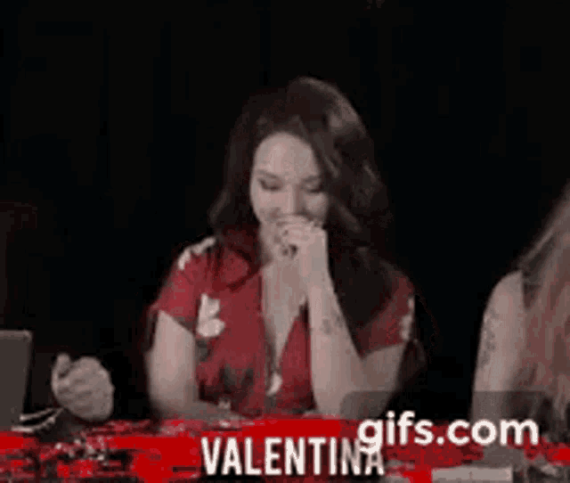 a woman in a red dress is sitting at a table in front of a sign that says valentina gifs.com .