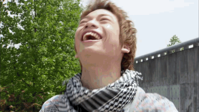 a young man wearing a scarf is laughing with his mouth wide open