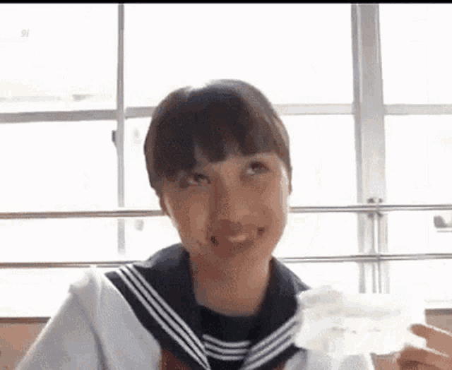 a girl in a sailor uniform is holding a piece of paper in her hand and smiling .