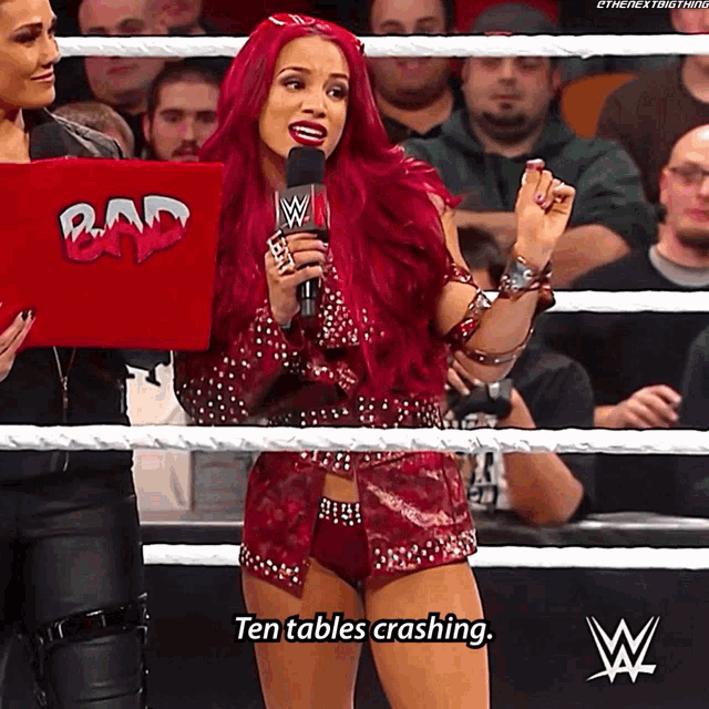 a woman in a wrestling ring holding a microphone and a sign that says bad