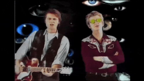 a man playing a guitar and another man singing in front of many eyes