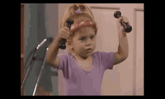a little girl is holding two dumbbells over her head .