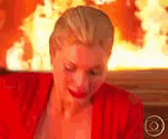 a woman in a red robe is sitting in front of a fireplace with flames behind her .