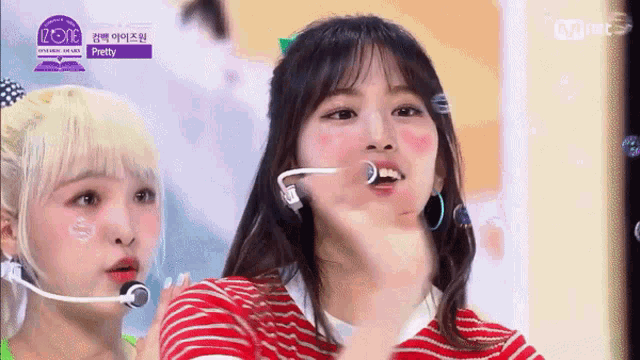 two girls are standing next to each other on a stage and one of them is wearing a red striped shirt .