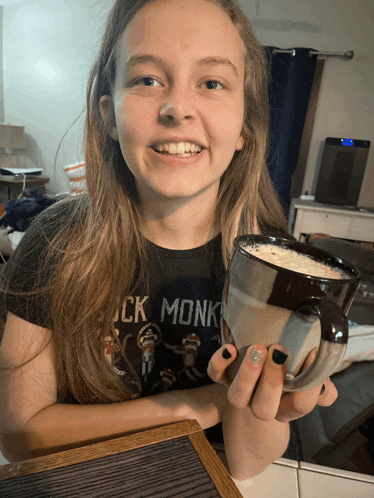 a girl wearing a black monk shirt holds a mug