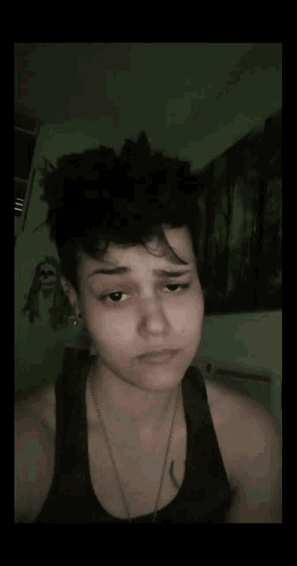 a woman with short hair is wearing a tank top and earrings .