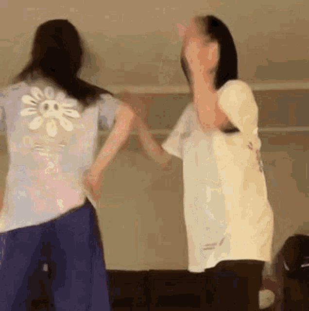 two women are dancing together in a room and one of them has a flower on her back .