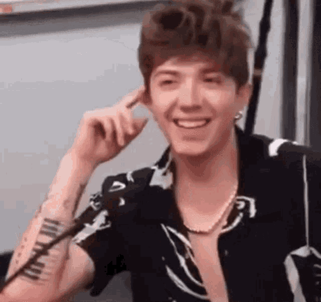 a young man wearing a striped shirt and a pearl necklace is smiling while talking on a cell phone .