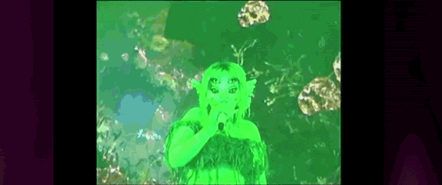 a green alien with many eyes is holding a microphone in front of a green background .