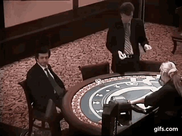 a man in a suit and tie stands in front of a roulette table with a woman sitting at it