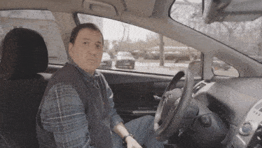 a man in a plaid shirt sits in the driver 's seat of a toyota car