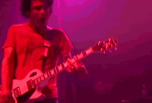 a man in a red shirt is playing a guitar in the dark