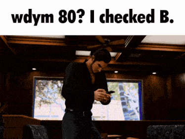 a man standing in a room looking at his phone with the words wdym 80 i checked b. below him