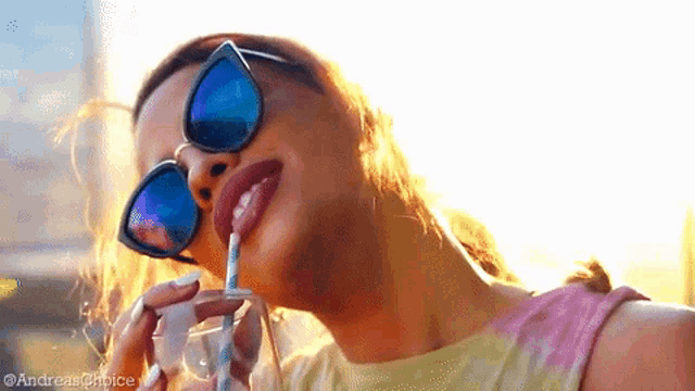 a woman wearing sunglasses is drinking from a straw