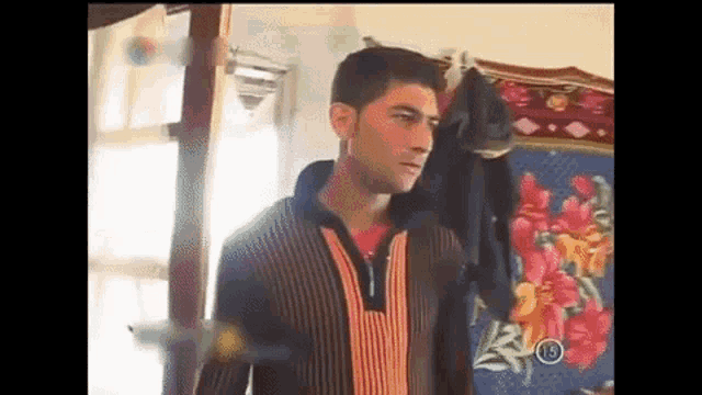 a man in a striped sweater is standing in a room in front of a floral rug .