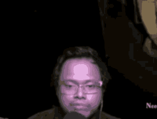 a man wearing glasses is talking into a microphone .