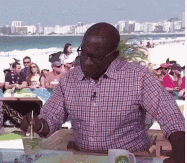 a man in a plaid shirt is sitting at a table with a drink in front of a crowd of people