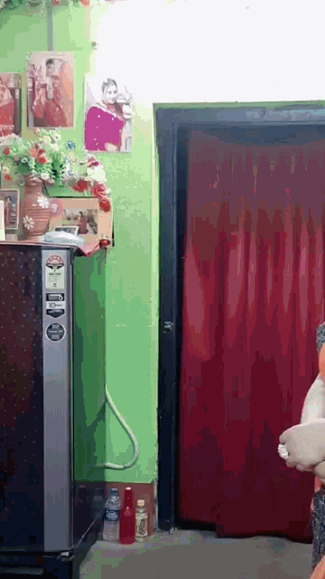 a woman is standing in a room with a red curtain and a black refrigerator .