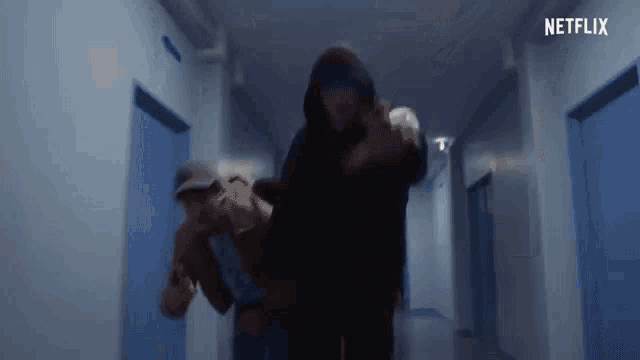 a man in a hooded jacket is carrying a woman in a hallway .