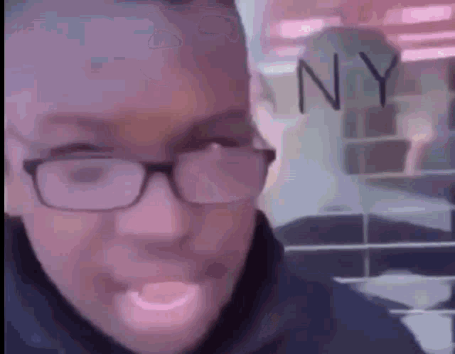 a man wearing glasses is standing in front of a sign that says ny .