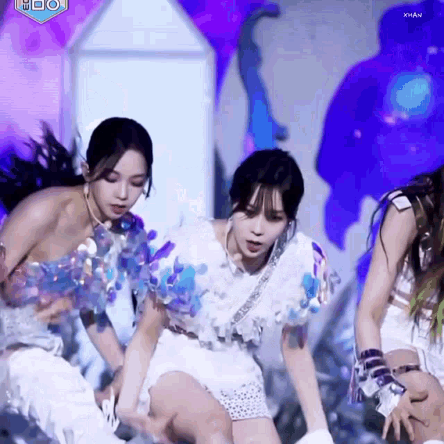 a group of women are dancing on a stage with a purple background