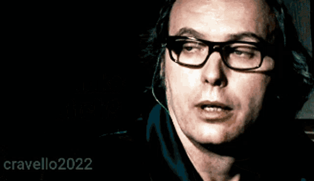 a man with glasses and a ring on his finger is talking on a phone with the year 2022 on the bottom