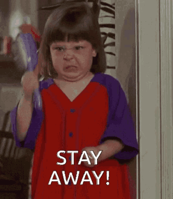 a little girl in a red and purple dress is holding a comb and saying stay away
