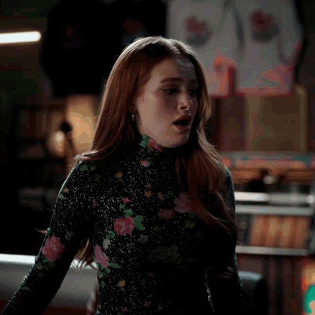 a woman wearing a black floral dress stands in front of a jukebox