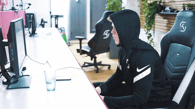 a man in a hoodie sits in front of a computer monitor