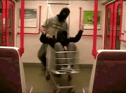 a man in a mask is pushing a woman in a shopping cart on a subway