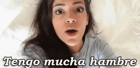 a woman is laying on a bed with her mouth open and the words `` tengo mucha hambre '' written on her face .