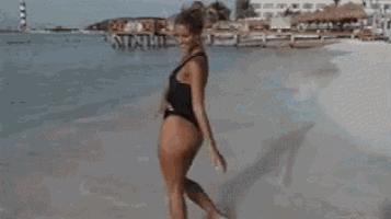 a woman in a black one piece swimsuit is standing on a beach .