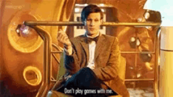 a man in a suit and bow tie is sitting in a chair holding a gun and talking to someone .