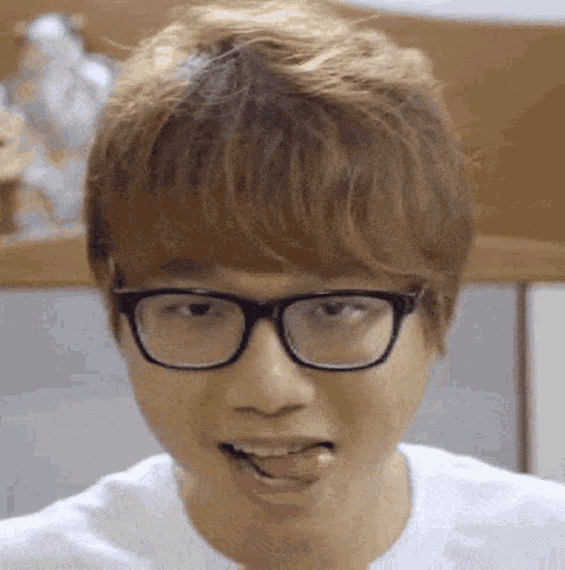 a young man wearing glasses and a white shirt is sticking his tongue out