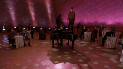a man standing on top of a piano in a room with people sitting at tables