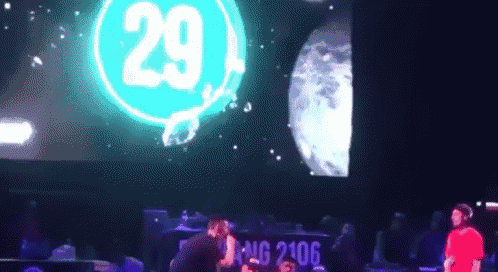 a man in a red shirt is standing in front of a large screen that says 29