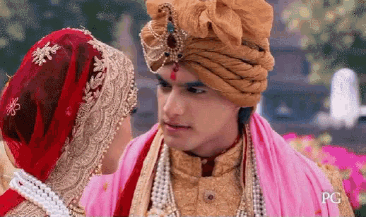 a bride and groom are looking at each other . the bride is wearing a red turban .